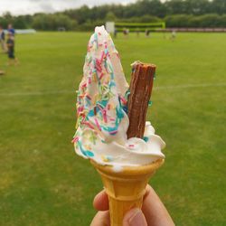 Cropped hand holding ice cream cone on field