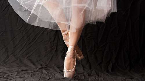 Low section of female ballet dancer dancing against black backdrop