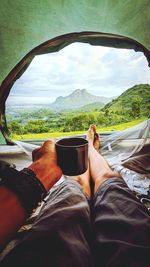 Low section of man relaxing on mountain against sky