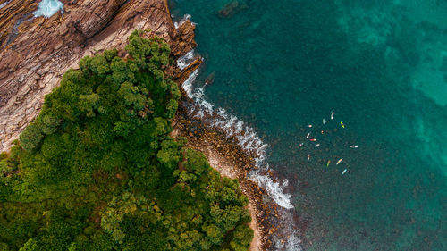 Tropical coast, ocean and waves crashing against rocks with surfers, drone shot, exotic landscape.