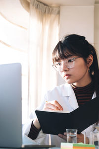 Scientist writing in book while looking at laptop at laboratory