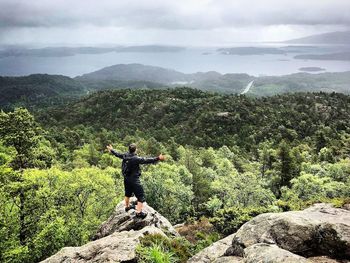 Rear view of man standing on rock against sky