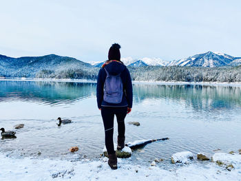 Rear view of man standing by lake against sky