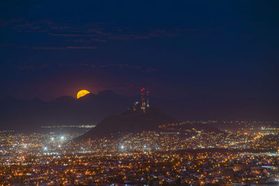 High angle view of illuminated buildings in city at night with full moon