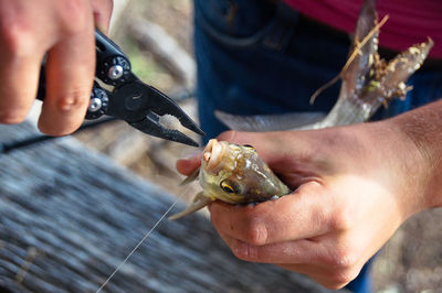 Midsection of man using pliers on fish outdoors