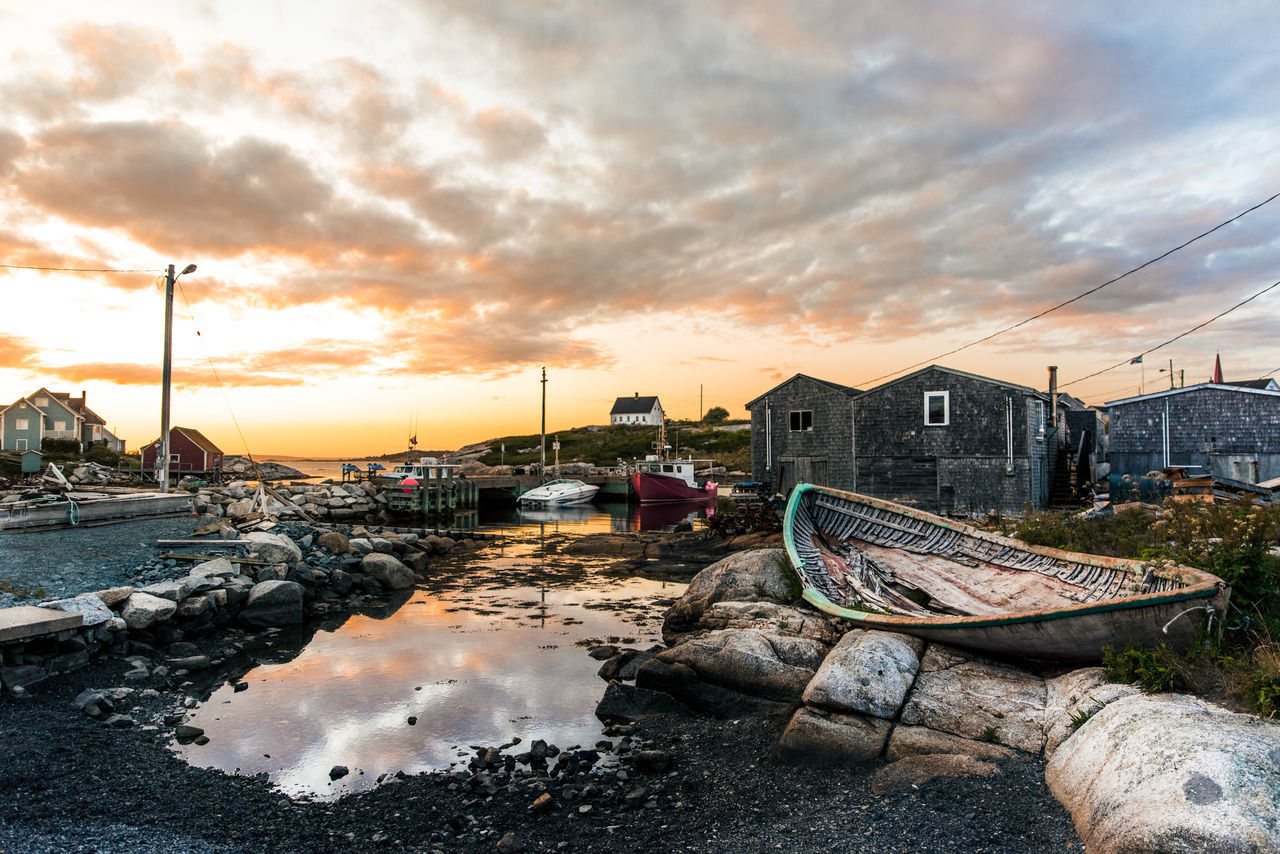 BOATS MOORED ON SEA AGAINST BUILDINGS AT SUNSET