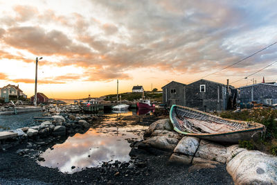 Boats moored on sea by buildings against sky during sunset