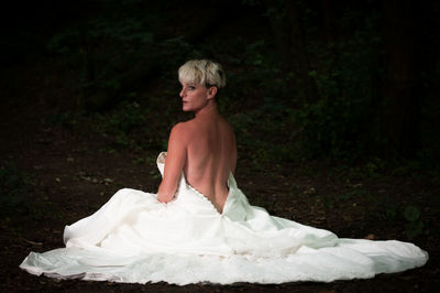 Bride wearing backless wedding dress sitting in forest