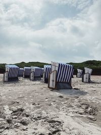 Hooded chairs on sand at beach against sky