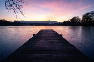 Pier over lake against sky during sunset