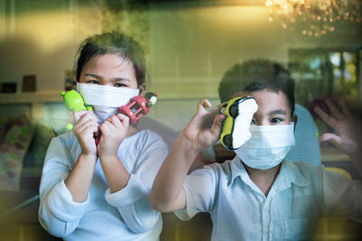 Portrait of sibling wearing mask holding toy