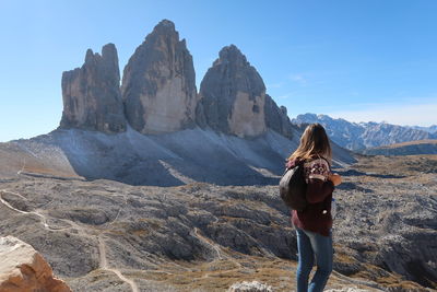 Side view of woman with backpack standing on mountain against sky