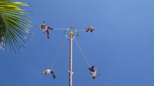Low angle view of people hanging on amusement park ride against clear blue sky