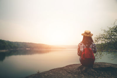 Woman standing by lake against sky during sunset