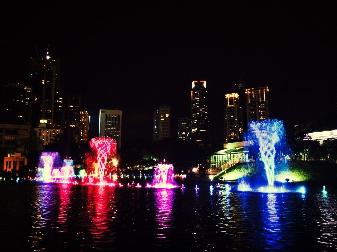 illuminated, building exterior, night, water, city, architecture, built structure, waterfront, cityscape, skyscraper, reflection, urban skyline, river, modern, clear sky, city life, office building, fountain, building, outdoors