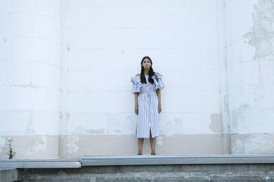 Portrait of young woman standing against white wall
