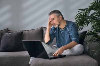 Young man using laptop while sitting on sofa at home