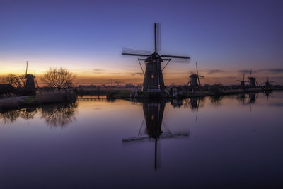 Traditional windmill by lake against sky during sunset