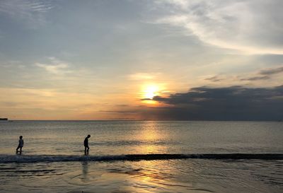 Silhouette people on beach against sky during sunset