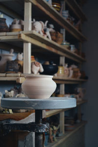 Clay pot close-up in the foreground and shelves with pottery - on the second