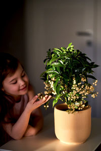 A girl looks at a home plant with berries in a clay pot.