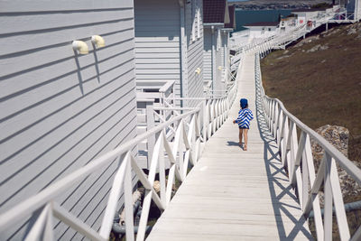 Boy child in a striped blue sailor jacket walks on the street among white wooden houses by the sea