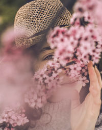 Close-up portrait of young woman with cherry blossoms wearing hat at park