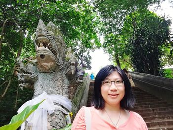 Portrait of smiling young woman statue against trees