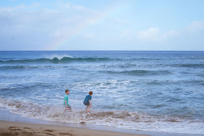 Young boys playing in the waves with a rainbow over the ocean on ka'anapali beach in hawaii. 