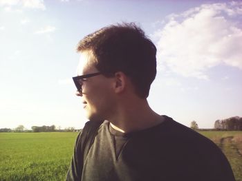 Portrait of young man looking away on field against sky