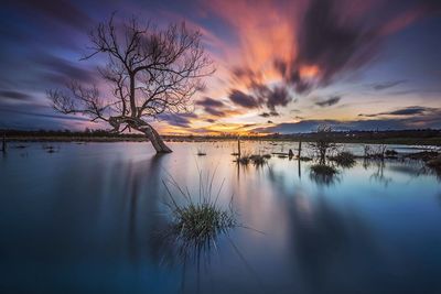 Scenic view of lake against dramatic sky at sunset