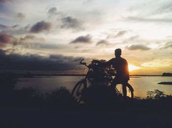 Silhouette man riding bicycle by sea against sky during sunset