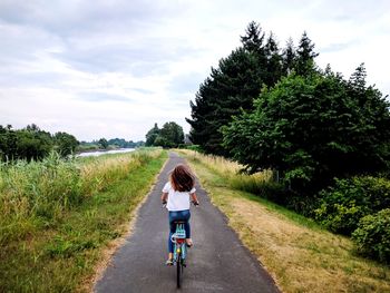 Rear view of woman riding bicycle on road against sky