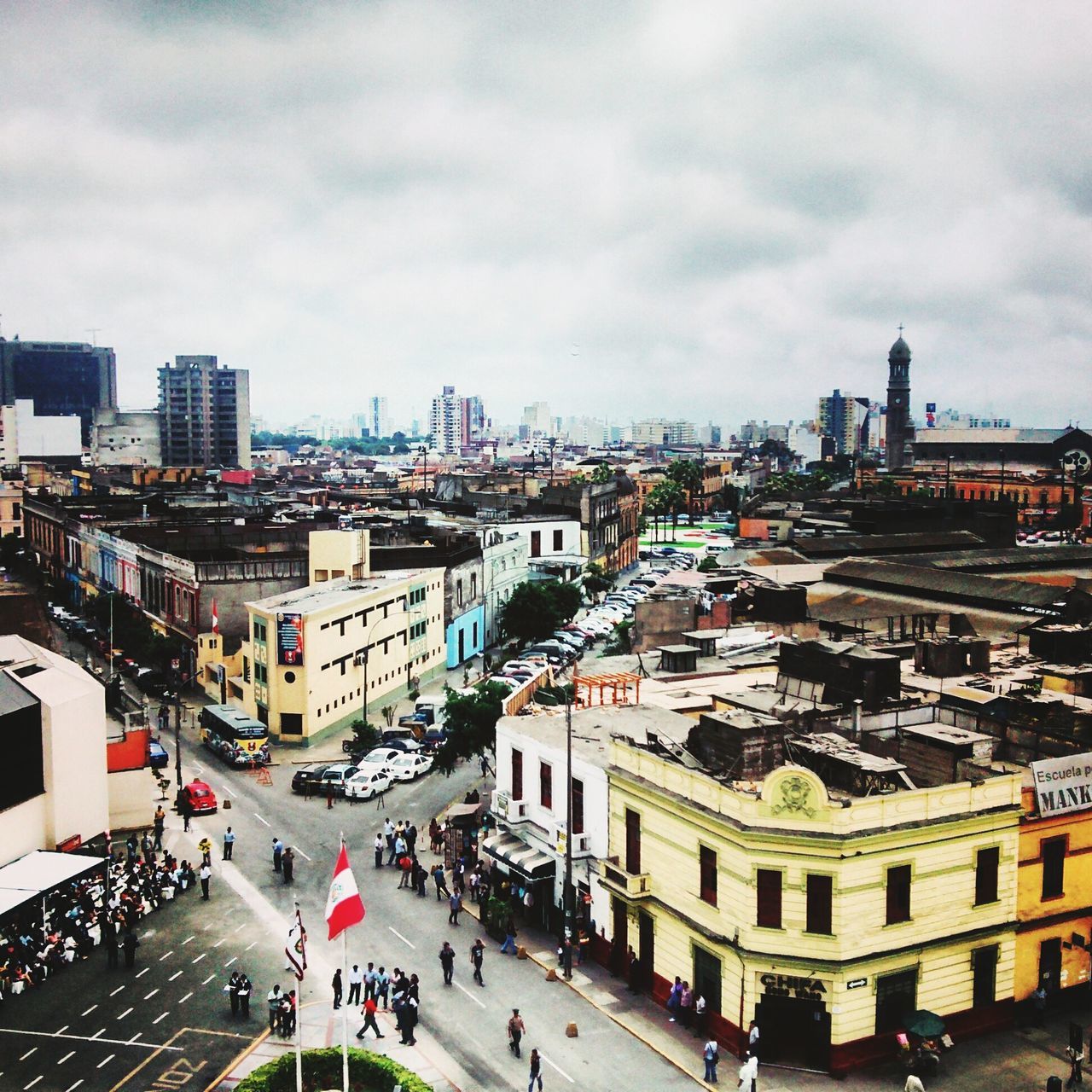 architecture, building exterior, built structure, city, transportation, street, car, land vehicle, large group of people, high angle view, sky, city life, road, mode of transport, city street, cloud - sky, cityscape, men, person