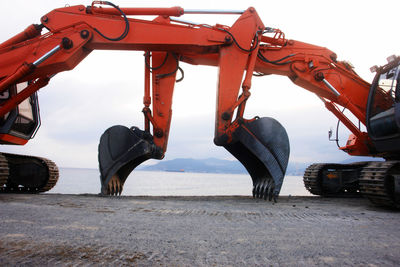 Diggers at beach against cloudy sky