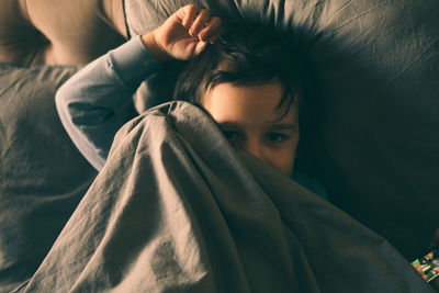 A little boy hides under the covers in bed and smiles.