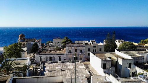 Buildings by sea against clear blue sky