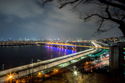 Illuminated bridge over river by buildings in city at night