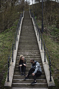 Multi-ethnic couple talking while sitting on steps after workout in forest