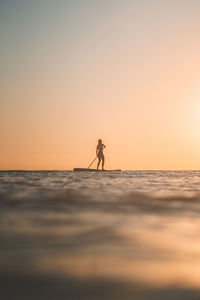 Silhouette man standing by sea against sky during sunset