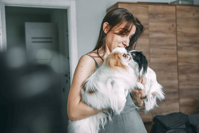 Woman tenderly holding two japanese chin dogs, showcasing affection and pet care at home