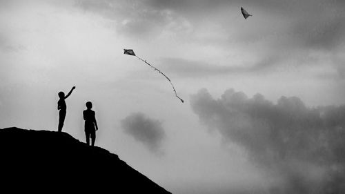 Low angle view of silhouette boys flying against sky