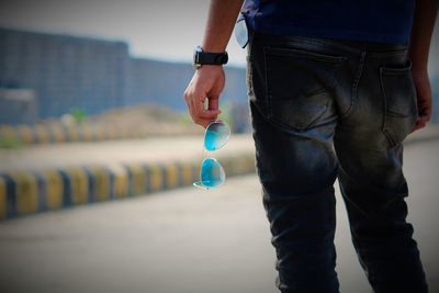 Midsection of man holding sunglasses on road