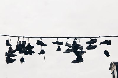 Low angle view of shoes hanging on rope against sky