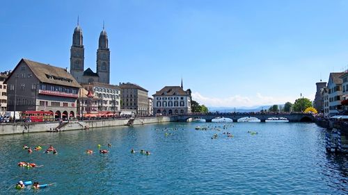 People enjoying in limmat river by buildings against blue sky