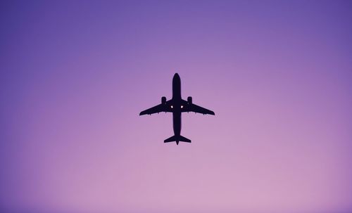 Directly below shot of silhouette airplane flying in clear purple sky