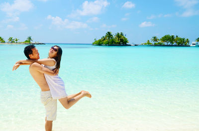 Man carrying woman while standing in sea against sky