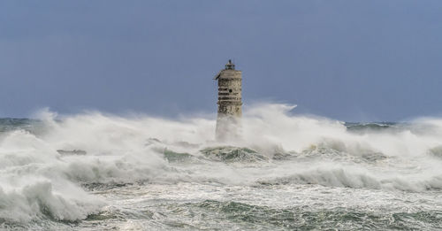 Lighthouse amidst sea and buildings against sky