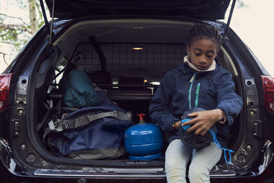 Girl sitting with camping gear in car trunk