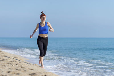 Woman running at beach against clear blue sky